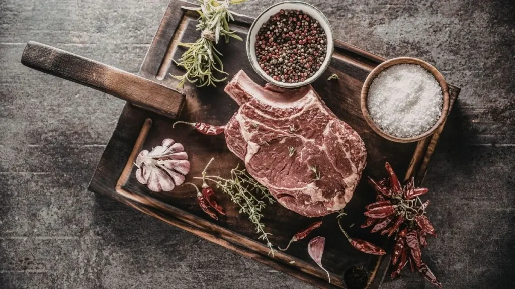 Corte de carne Cowboy sobre tabla de madera con sal de mar romero y pimienta negra
